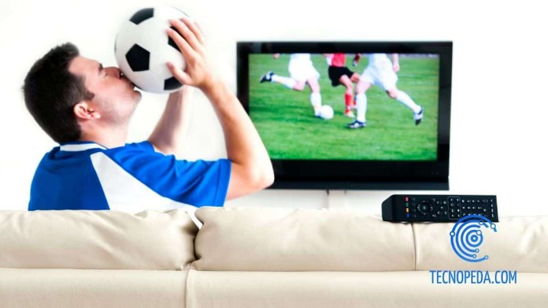 Hombre besando un balón y viendo el fútbol por tv